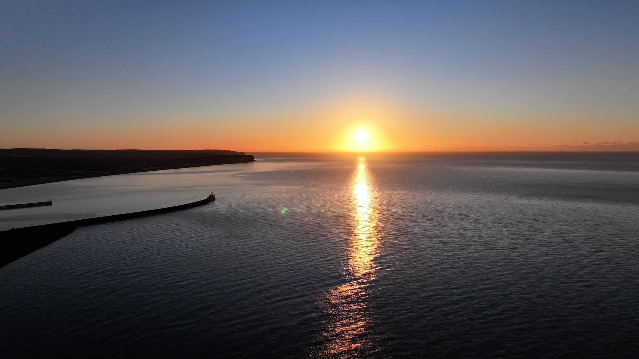 Un atardecer sobre una masa de agua tranquila con un muelle que se adentra en el agua.