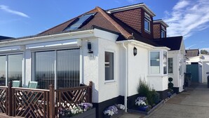 A white house with a brown roof, large windows, and a wooden deck. - The Beach House Peacehaven, Brighton, East Sussex with free parking onsite (Peacehaven)
