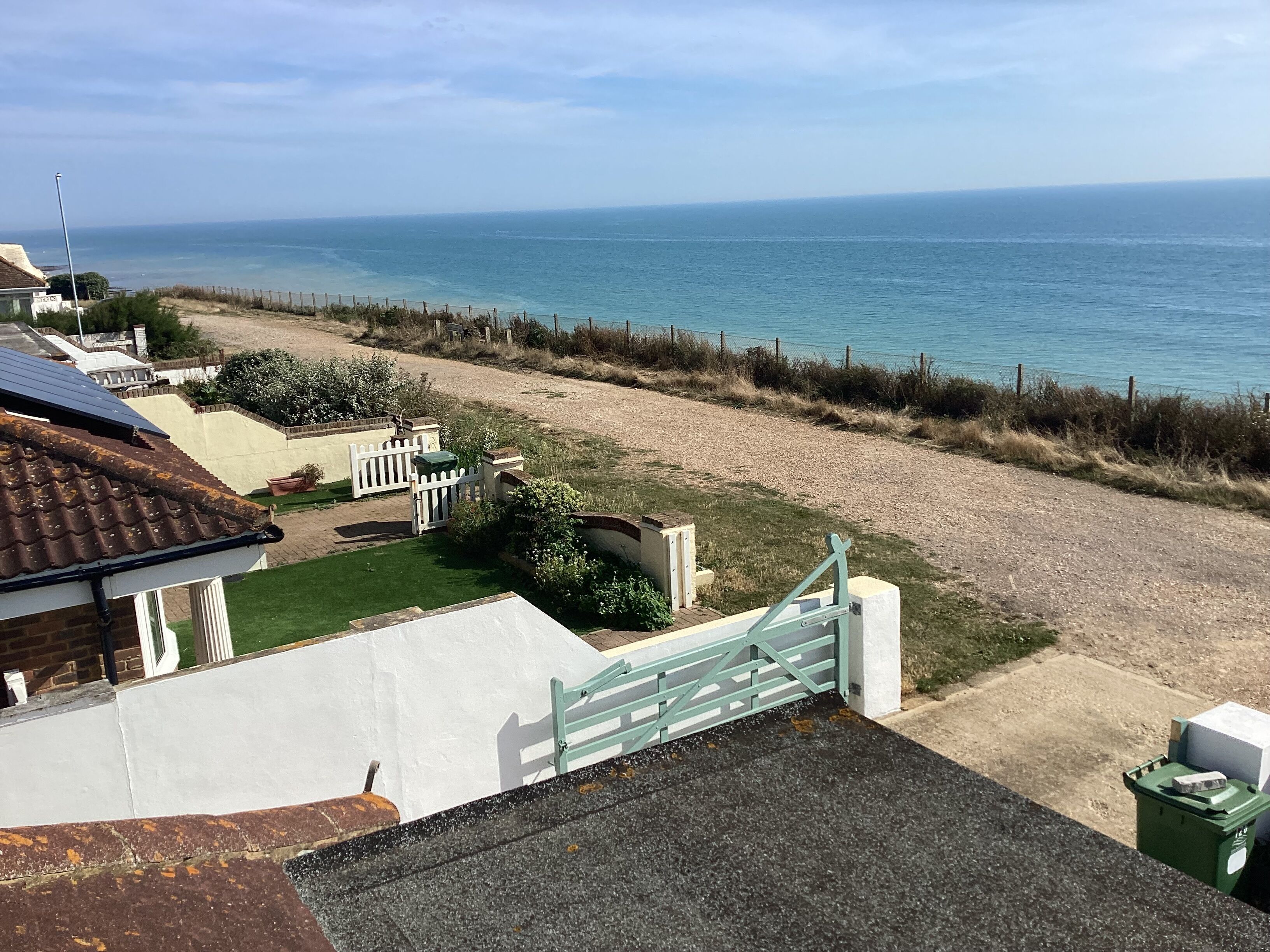 Une propriété située en bord de mer, dotée d’une allée pavée, d’un portail blanc et offrant une vue sur la mer.