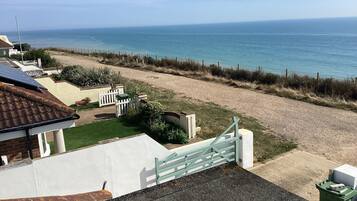 Une propriété située en bord de mer, dotée d’une allée pavée, d’un portail blanc et offrant une vue sur la mer.