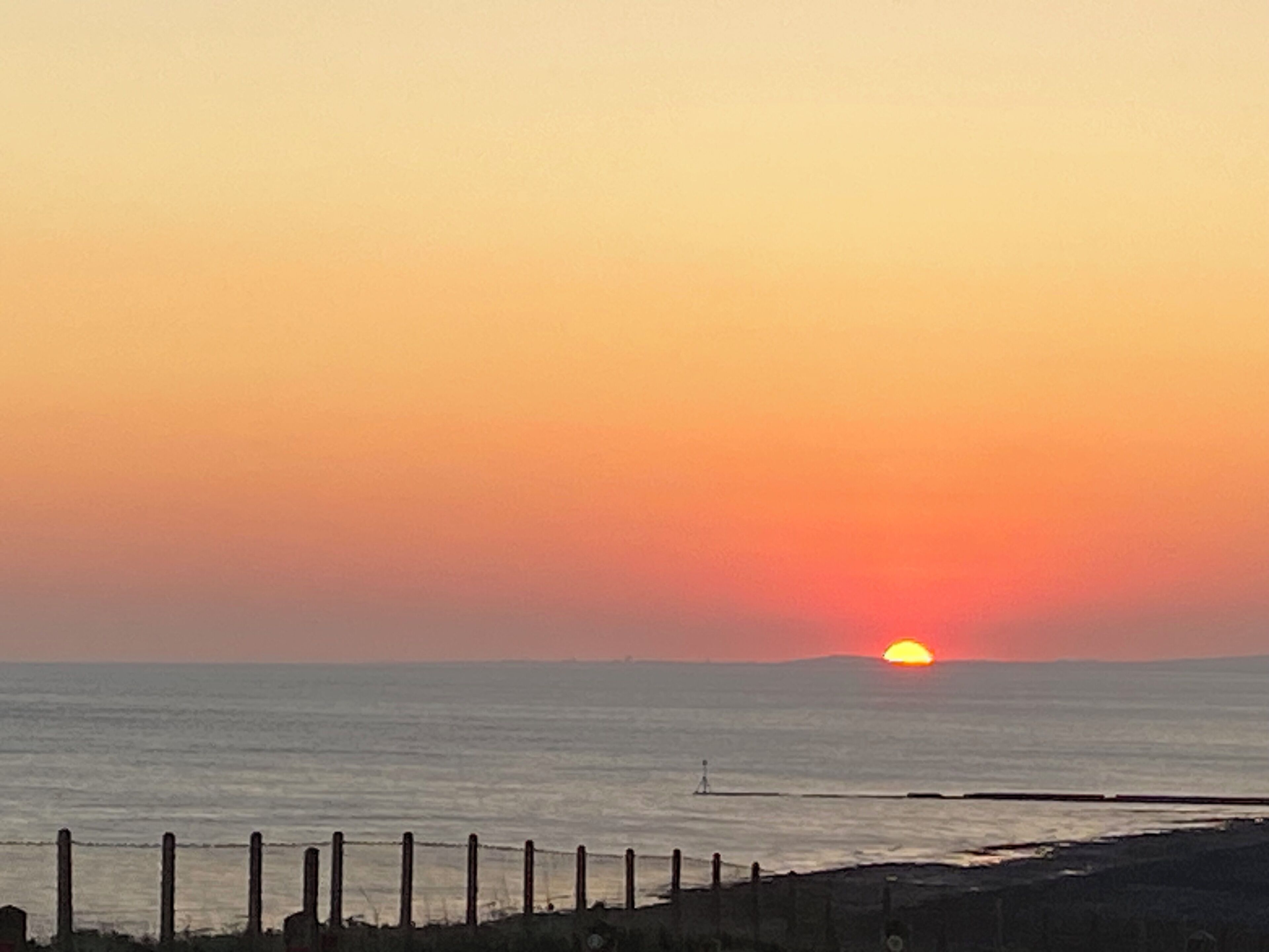 Tramonto sull'oceano con una recinzione di legno in primo piano.