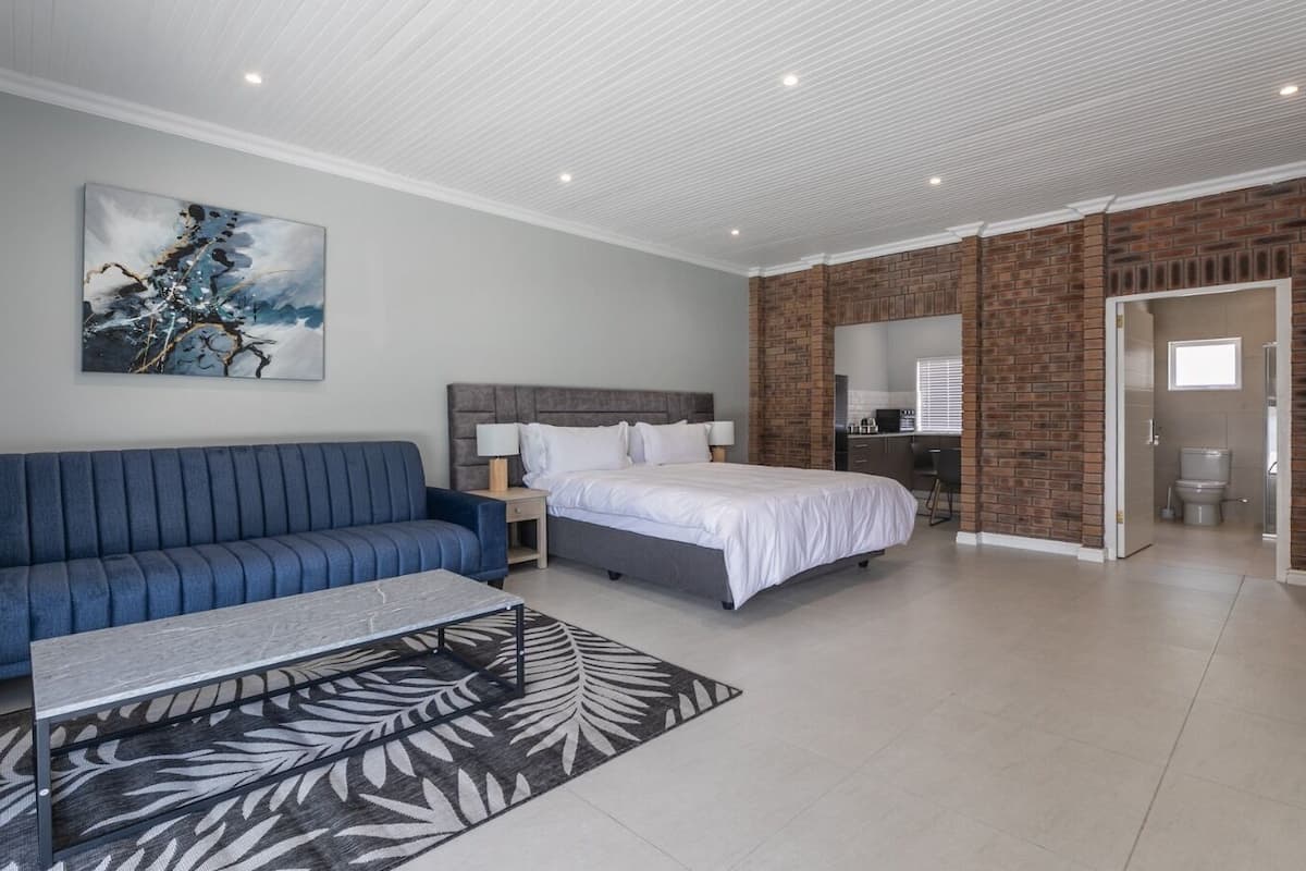 A modern bedroom with a blue sofa, a bed, a desk, and a bathroom visible through an open door.