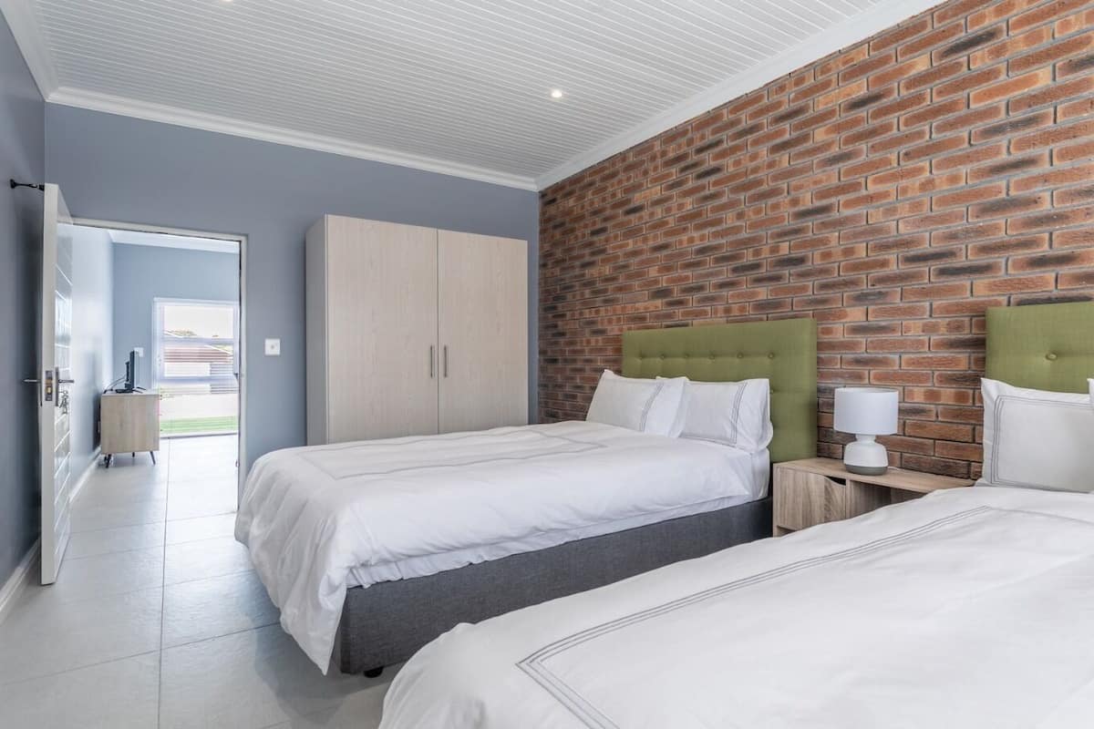 A hotel room with two beds, a green headboard, a brick wall, and a white ceiling.