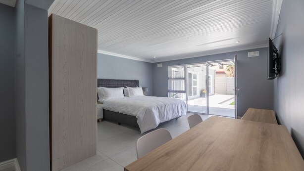 A modern bedroom with a bed, a wooden table, and a TV mounted on the wall. - Inkantu Apartments & Suites (Cape Town)