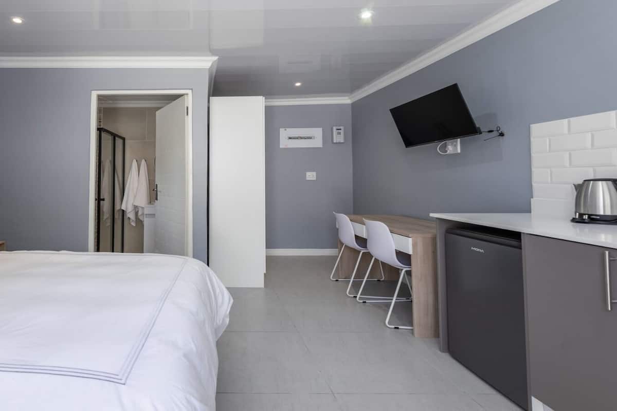 A modern hotel room with a large bed, a desk with chairs, a television, and a kitchenette.