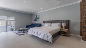 A modern bedroom with a large bed, a blue sofa, a small table, and a nightstand. - Inkantu Apartments & Suites (Cape Town)