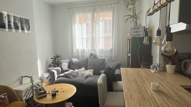 A modern living room with a sofa, coffee table, and a wooden dining table.