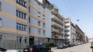 A multi-story residential building with balconies and a row of parked cars on the street. - Easylife - Fantastic studio in Risorgimento area (Milano)