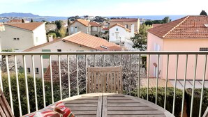 A balcony with a wooden table and a chair, overlooking a residential area with houses and a clear sky.