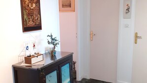 A hallway with a marble floor, a dark wooden cabinet with decorative panels, a framed painting, and a door with a light switch and a small plant.