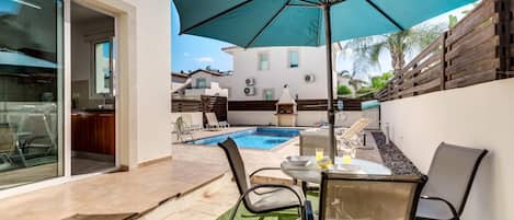 A patio with a pool, outdoor furniture, and a large umbrella.