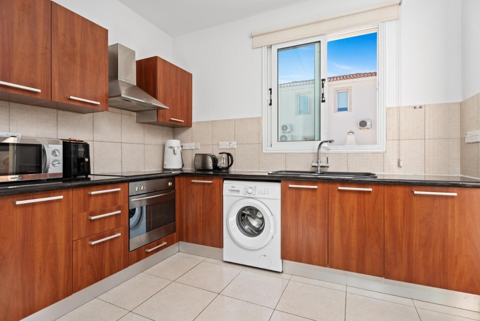 A modern kitchen with wooden cabinets, a built-in oven, microwave, coffee maker, and a washing machine.
