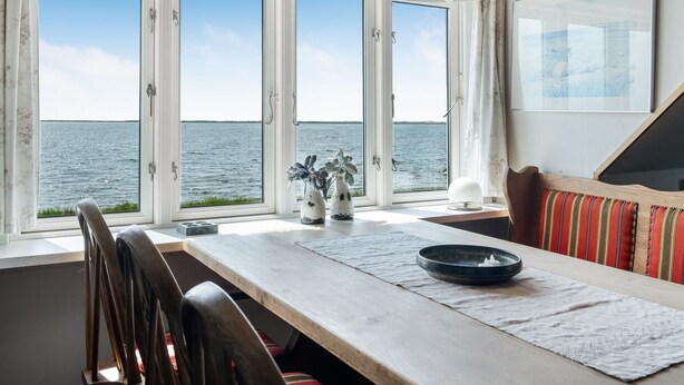 Un coin repas avec vue sur la mer, une table en bois, des chaises, un luminaire suspendu et un banc rembourré.