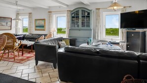 Un salon comprenant un canapé, des fauteuils, un meuble, un téléviseur et donnant sur l’extérieur.