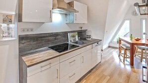 Eine moderne Küche mit Einbauherd, Kaffeemaschine und Spüle. Durch ein Fenster ist ein Essbereich mit Tisch und Stühlen zu sehen.