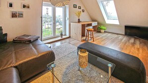 Eine moderne Lofts-Wohnung mit großem Fenster, Holzboden, einer Couch, einem Essbereich und einem Fernseher.