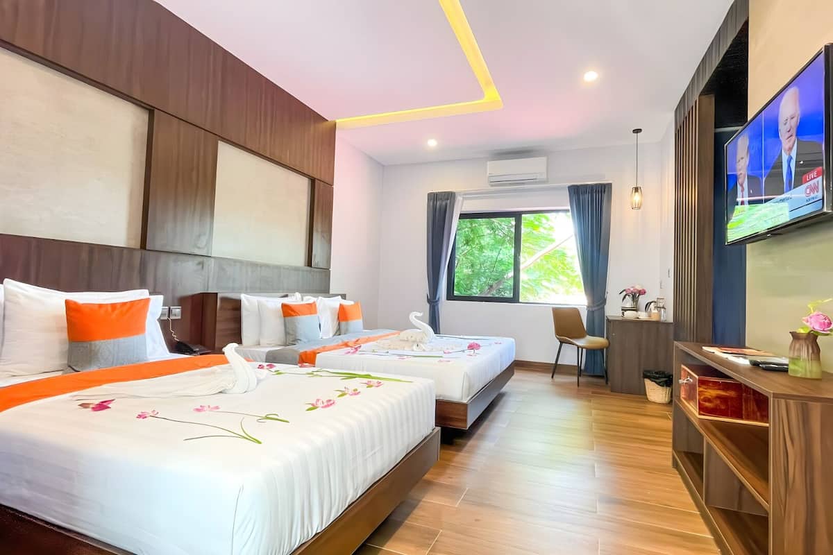 A hotel room with two beds, a TV, a desk, and a window with a view of greenery.