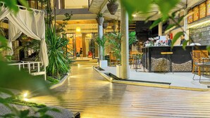 An indoor walkway with wooden flooring, potted plants, and seating areas. - The Luxury (Siem Reap)