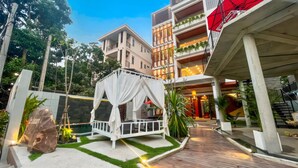 A modern hotel courtyard with a white gazebo, a stone sculpture, and a wooden deck. - The Luxury (Siem Reap)