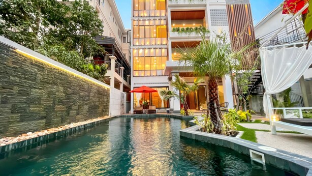 A modern hotel courtyard with a swimming pool, stone wall, and outdoor seating area. - The Luxury (Siem Reap)