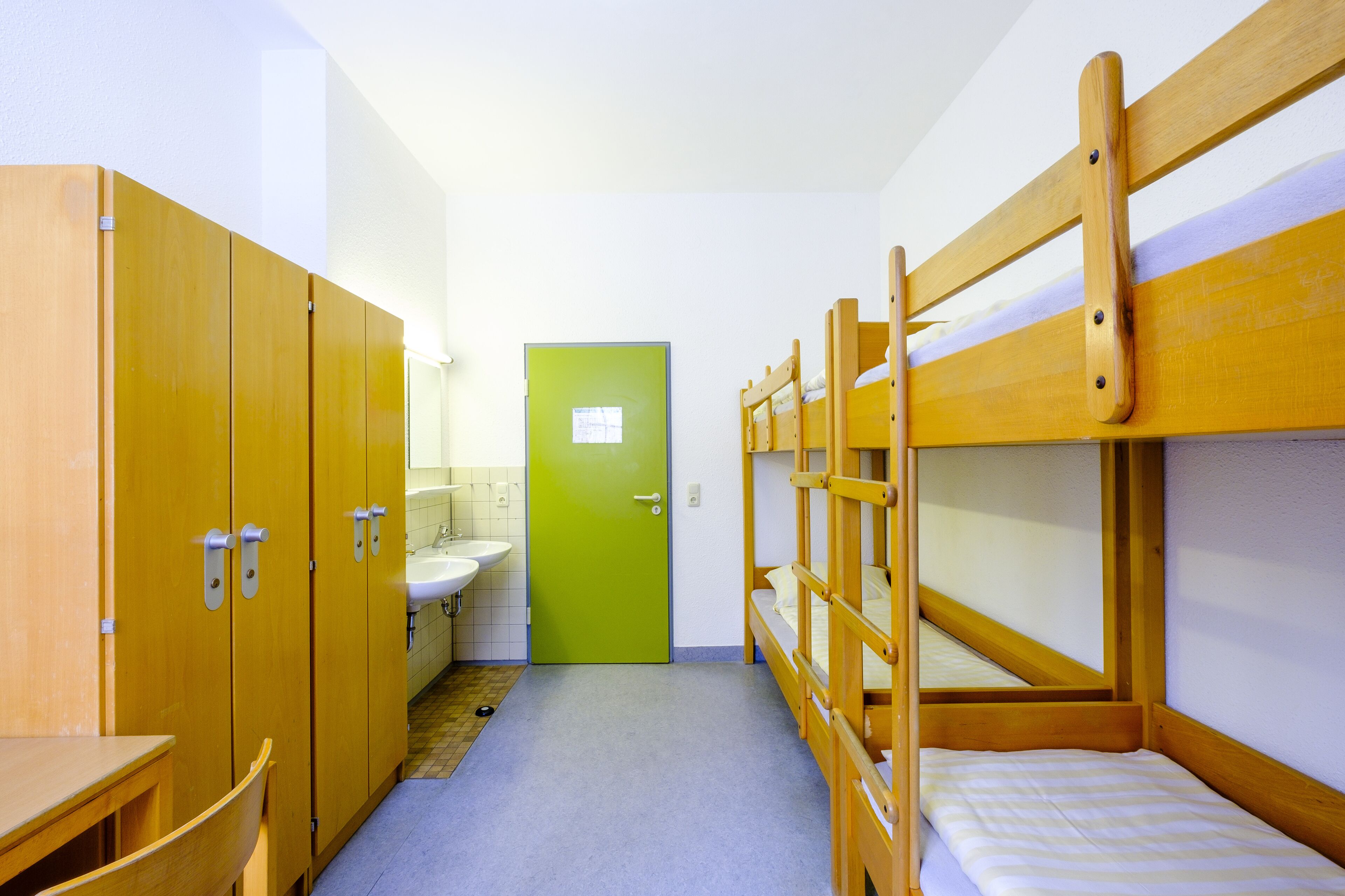 A dormitory room with bunk beds, a sink, and wooden cabinets.