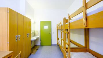 A dormitory room with bunk beds, a sink, and wooden cabinets.