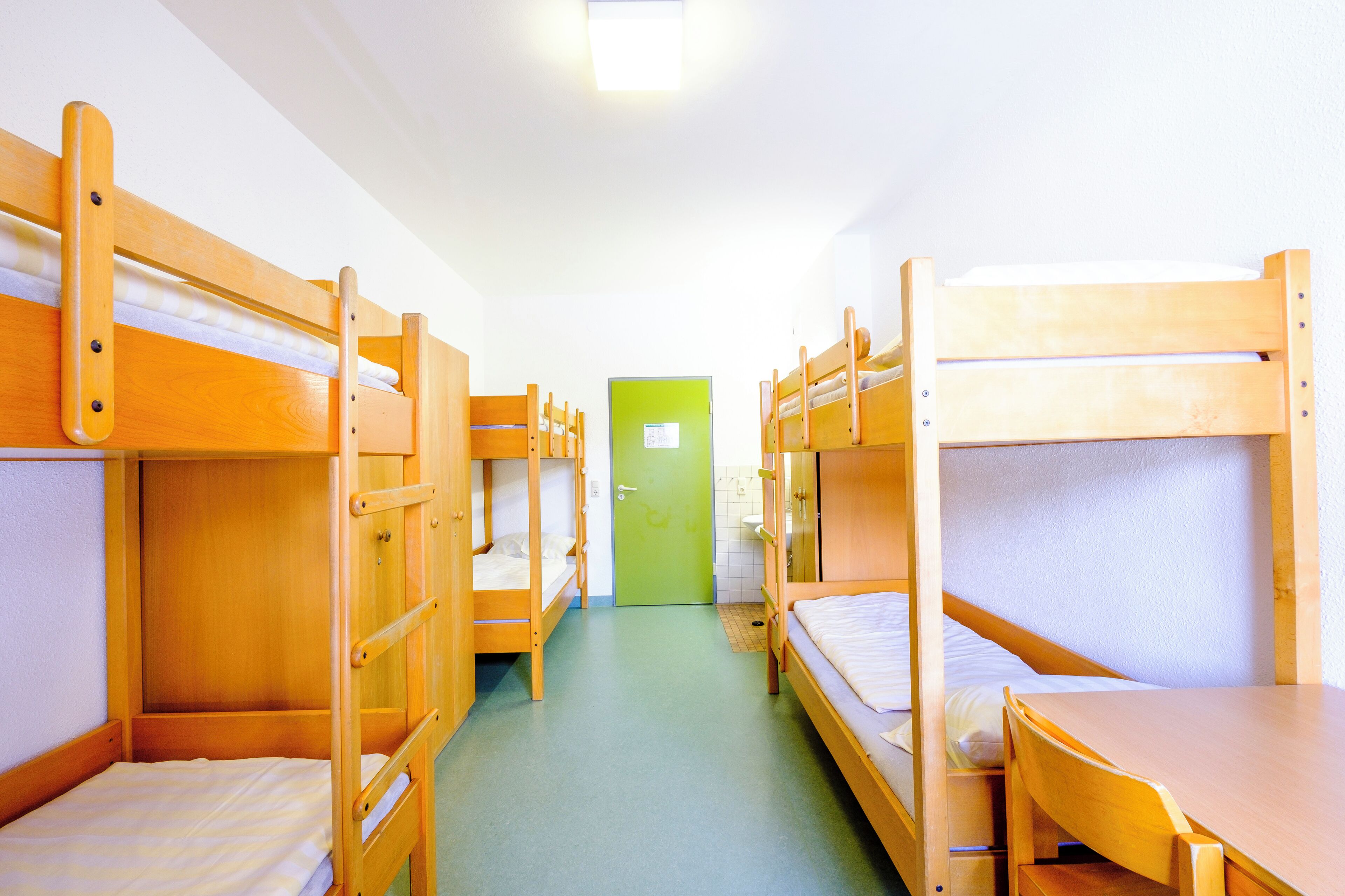 A dormitory room with bunk beds, a green door, and a tiled floor.