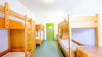 A dormitory room with bunk beds, a green door, and a tiled floor.