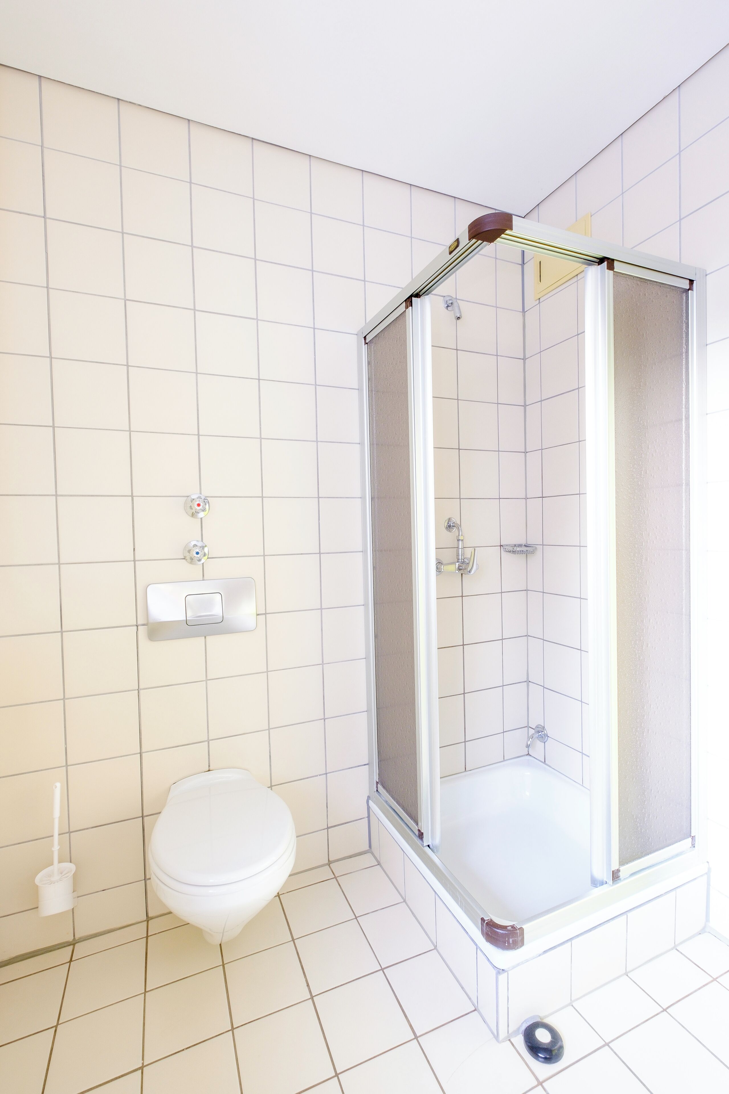 Un baño con inodoro blanco, cabina de ducha y dispensador de papel higiénico en la pared.