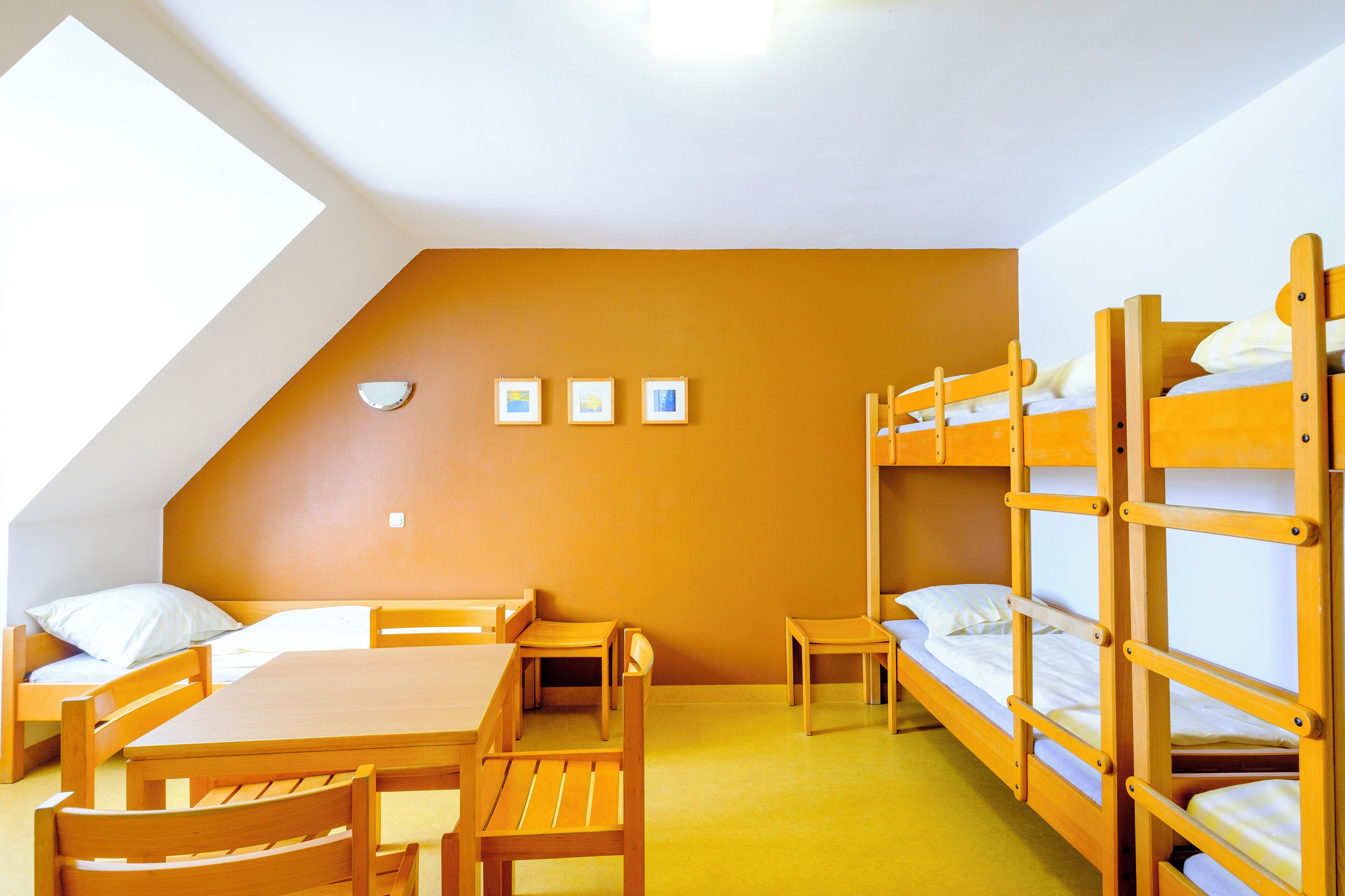 A dormitory room with bunk beds, a desk, chairs, and a small table.