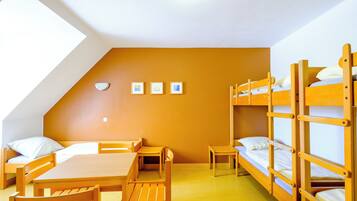 A dormitory room with bunk beds, a desk, chairs, and a small table.