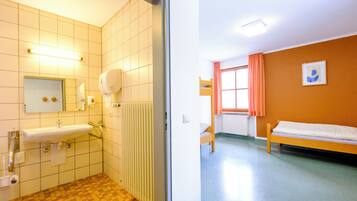 Ein Badezimmer mit Waschbecken, Spiegel und Toilette, sowie ein Schlafzimmer mit Bett und Fenster.