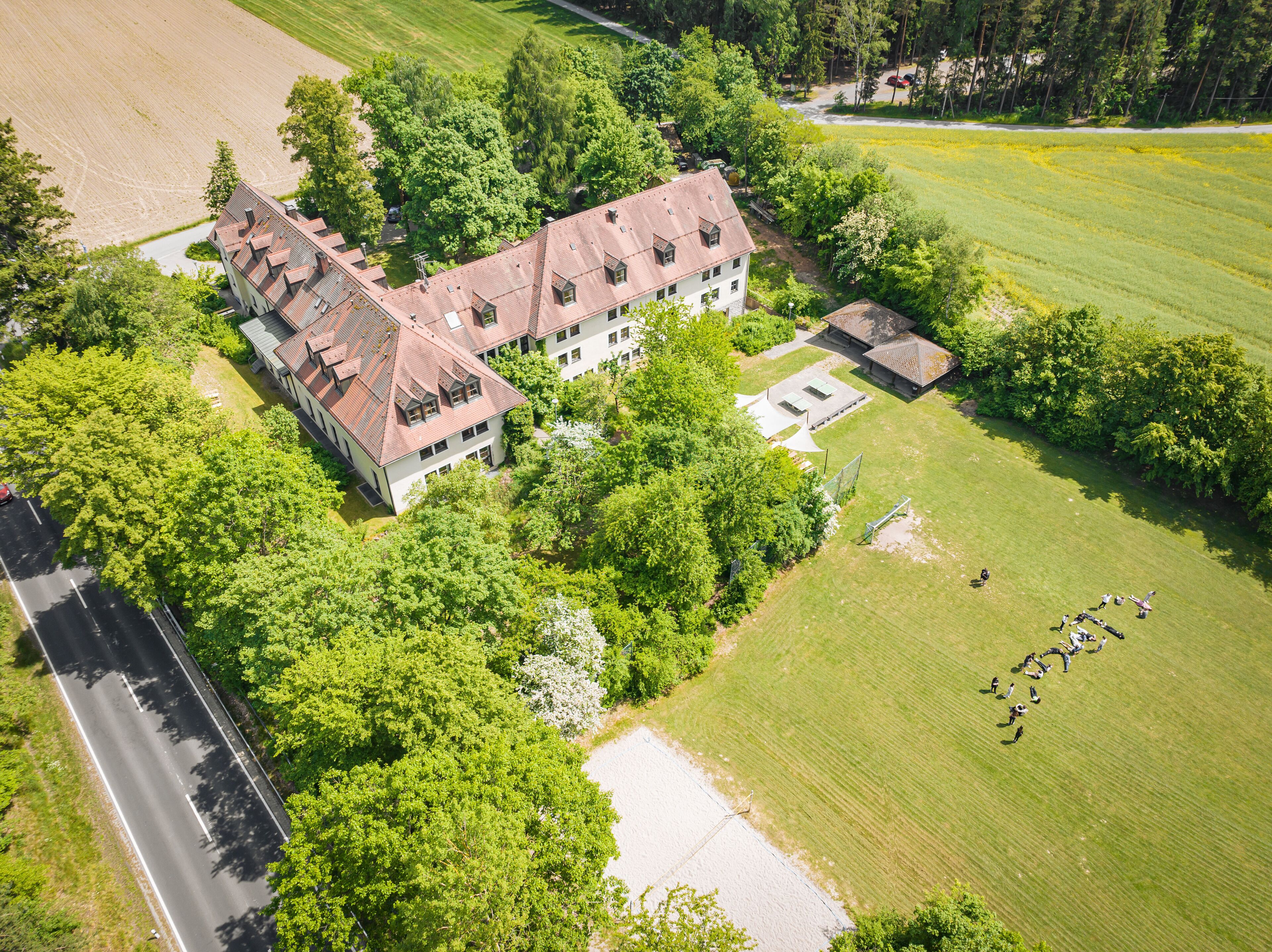 An aerial view of a large, multi-story building with a red-tiled roof, surrounded by lush greenery and a well-maintained lawn.