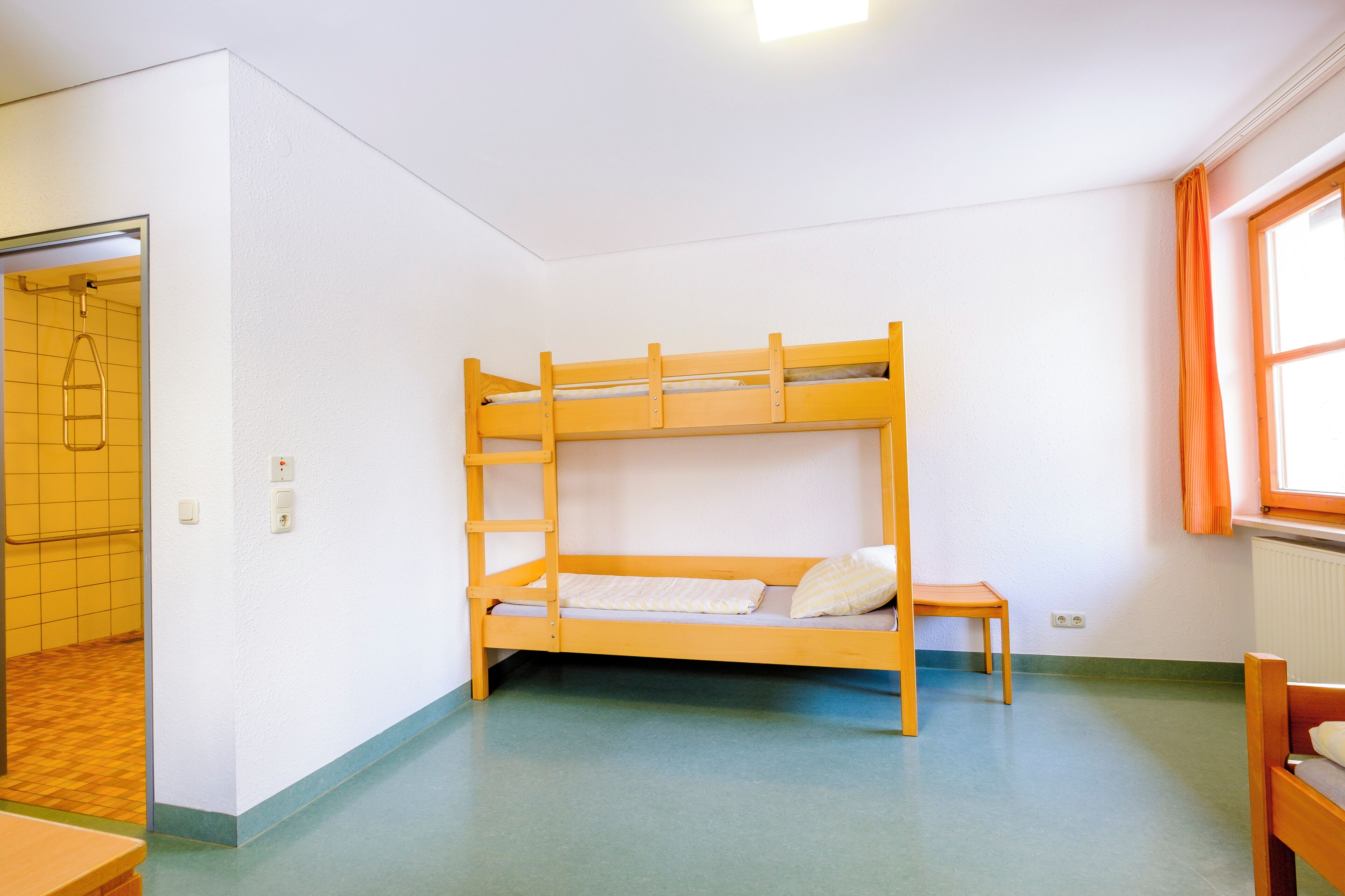A bunk bed room with a small table and a window with curtains.
