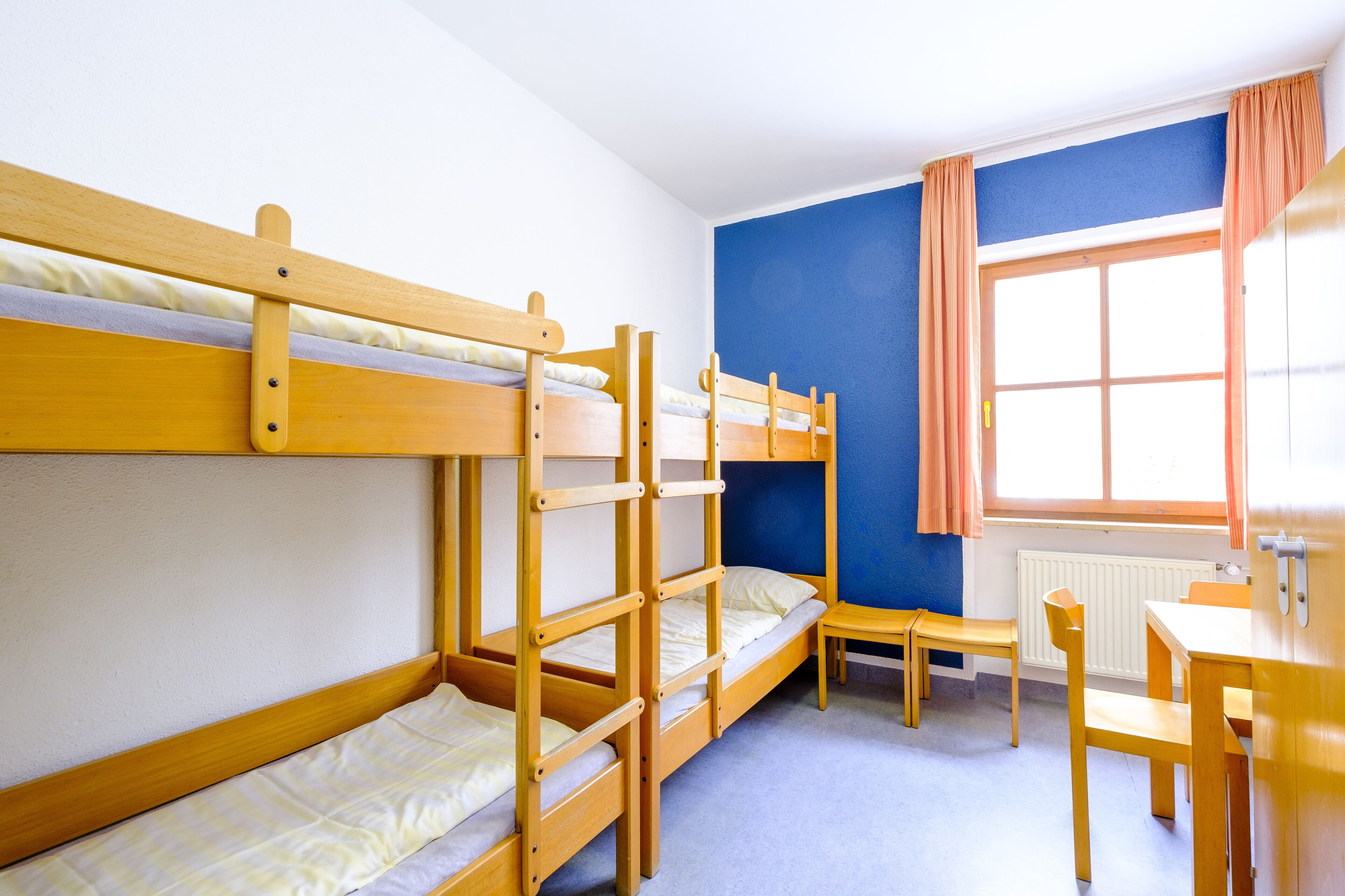 A bunk bed room with a desk and chair, a window with curtains, and a radiator.