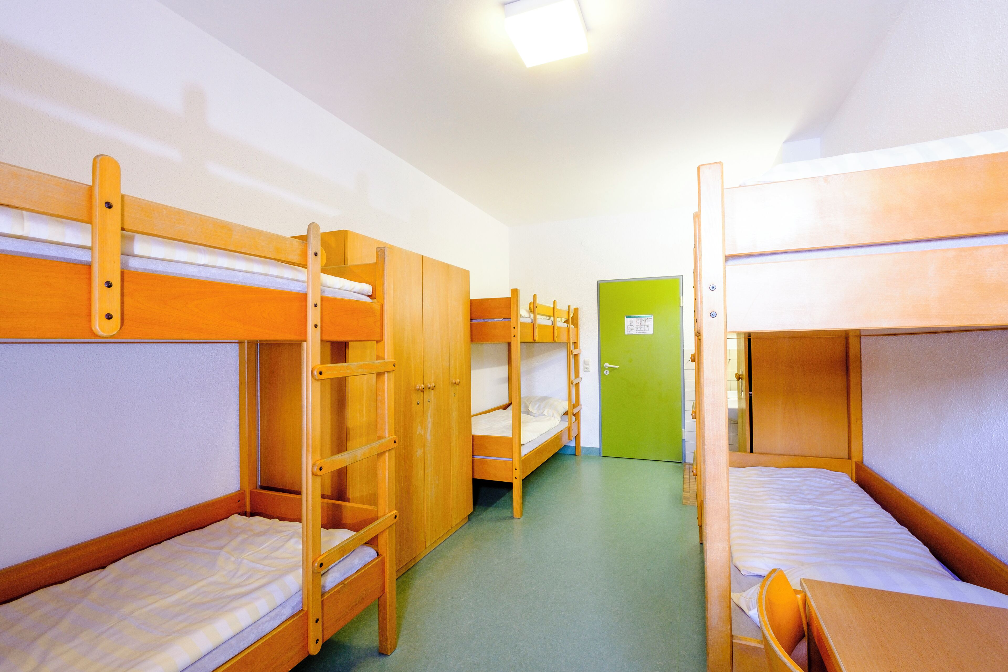 A dormitory room with bunk beds, a green door, and a wooden desk.
