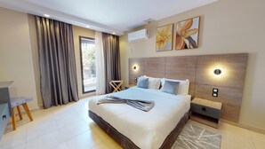 Moderni hotellihuone, jossa on suuri sänky, työpöytä ja tuoli. Huoneessa on verhot, ikkuna ja taideteoksia seinällä.