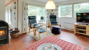 Una sala de estar acogedora con chimenea, dos sillones de cuero, un televisor y un amplio ventanal con vistas al exterior.