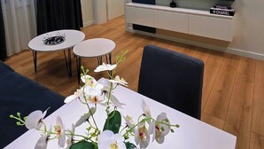 A modern living room with a flat-screen TV, a white dining table with a vase of orchids, and a blue sofa. - Arkle 2 Apartments  (Tirana)