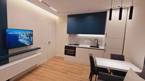 A modern kitchen with a built-in oven, a dining area with a table and chairs, and a TV mounted on the wall. - Arkle 2 Apartments  (Tirana)