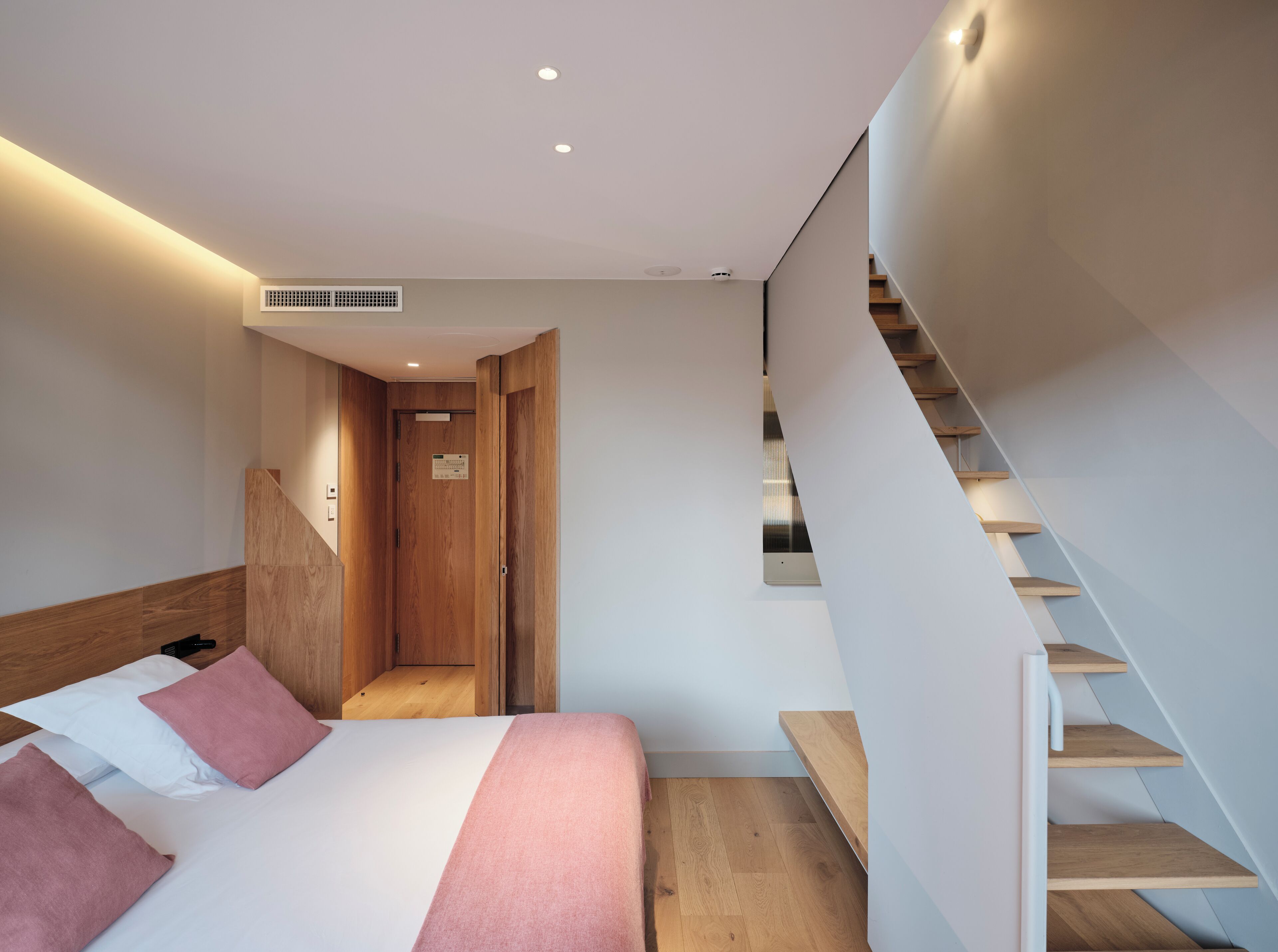 A modern bedroom with a bed, wooden headboard, and a staircase with wooden steps.