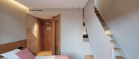 A modern bedroom with a bed, wooden headboard, and a staircase with wooden steps.