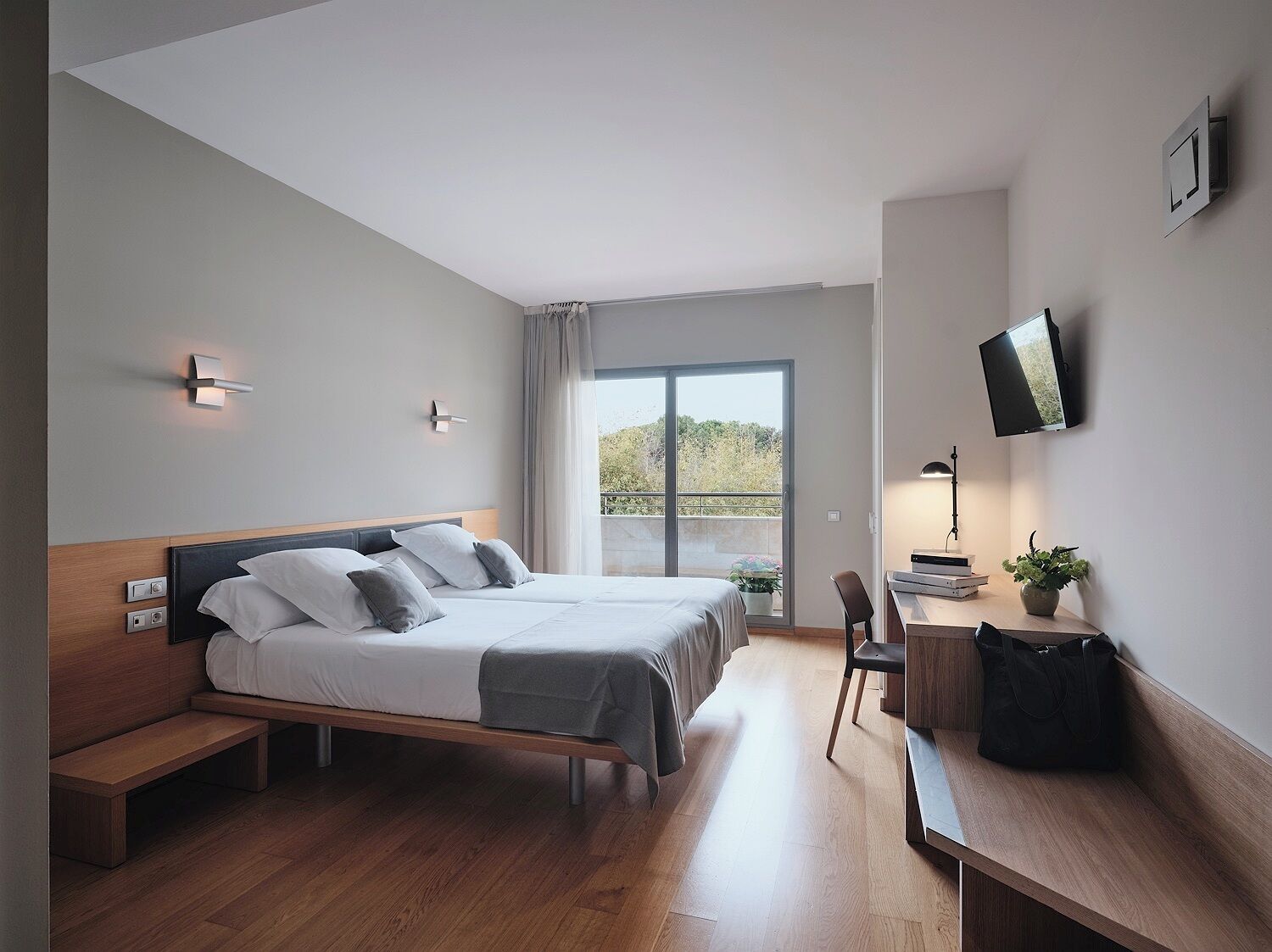 Habitación de hotel moderna con una cama grande, un escritorio con silla, televisor y balcón con vistas.