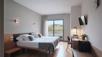 Habitación de hotel moderna con una cama grande, un escritorio con silla, televisor y balcón con vistas.