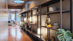 A modern interior with a long hallway, wooden flooring, and a series of shelves with various decorative items and a large plant. - Qgat Suites & Events (Sant Cugat del Valles)