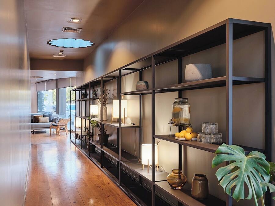 Un interior moderno con un largo pasillo, suelo de madera y una serie de estanterías con diversos objetos decorativos y una planta grande.