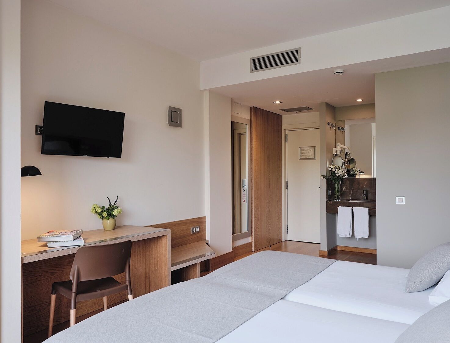 A hotel room with a bed, a desk, a chair, a television, and a bathroom visible through an open door.