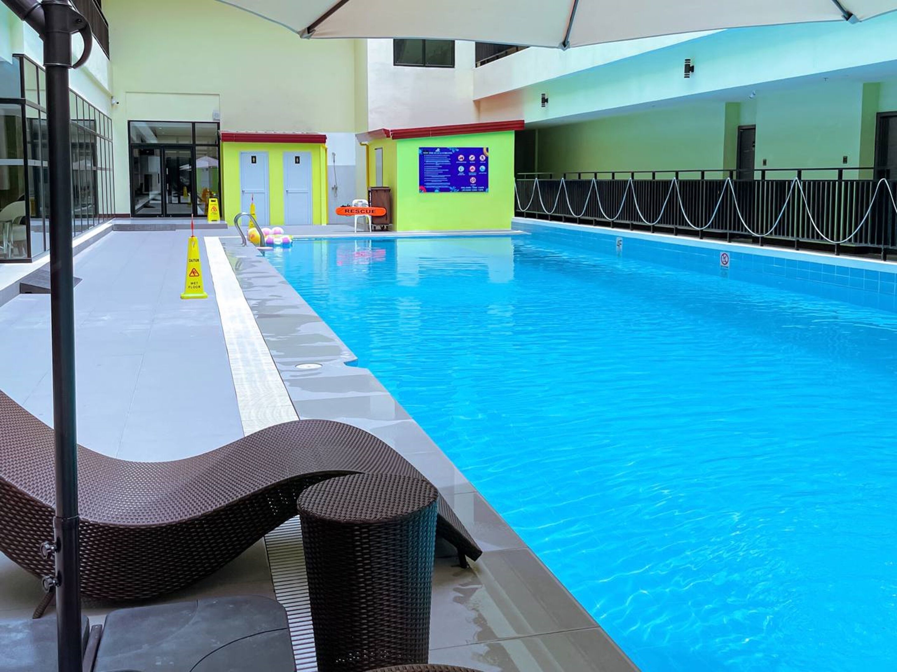 An indoor swimming pool with a clear water surface, a safety sign, and a lifeguard chair.