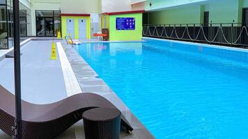 An indoor swimming pool with a clear water surface, a safety sign, and a lifeguard chair.
