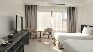Una habitación de hotel con dos camas, un escritorio con computadora, una silla y una ventana con cortinas.